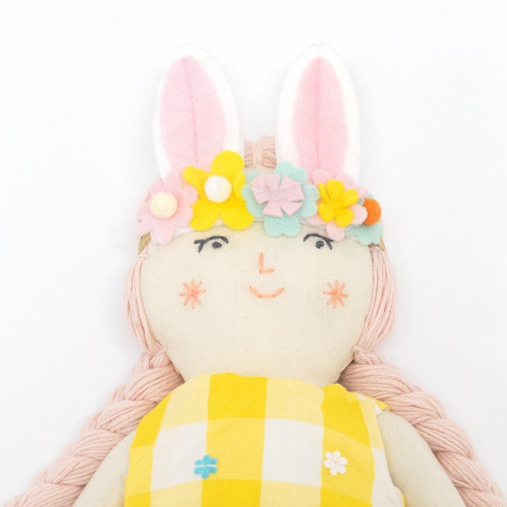 Alice is crafted from fabric, and is wearing a yellow gingham dress and a bunny ear headband. 