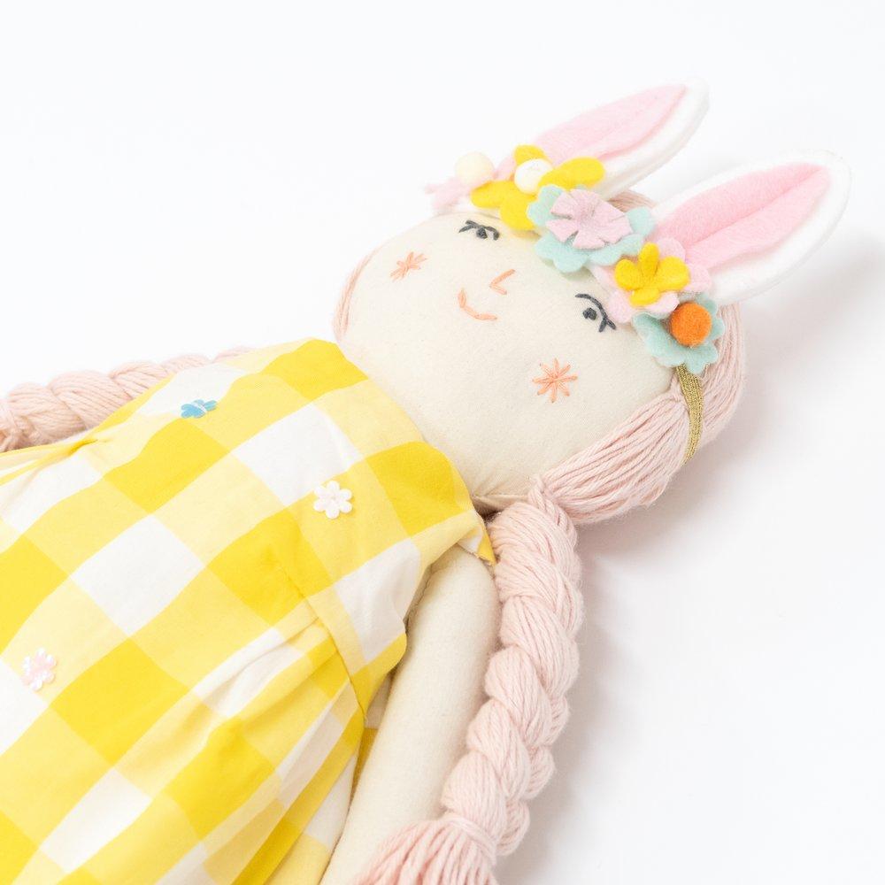 Alice is crafted from fabric, and is wearing a yellow gingham dress and a bunny ear headband. 