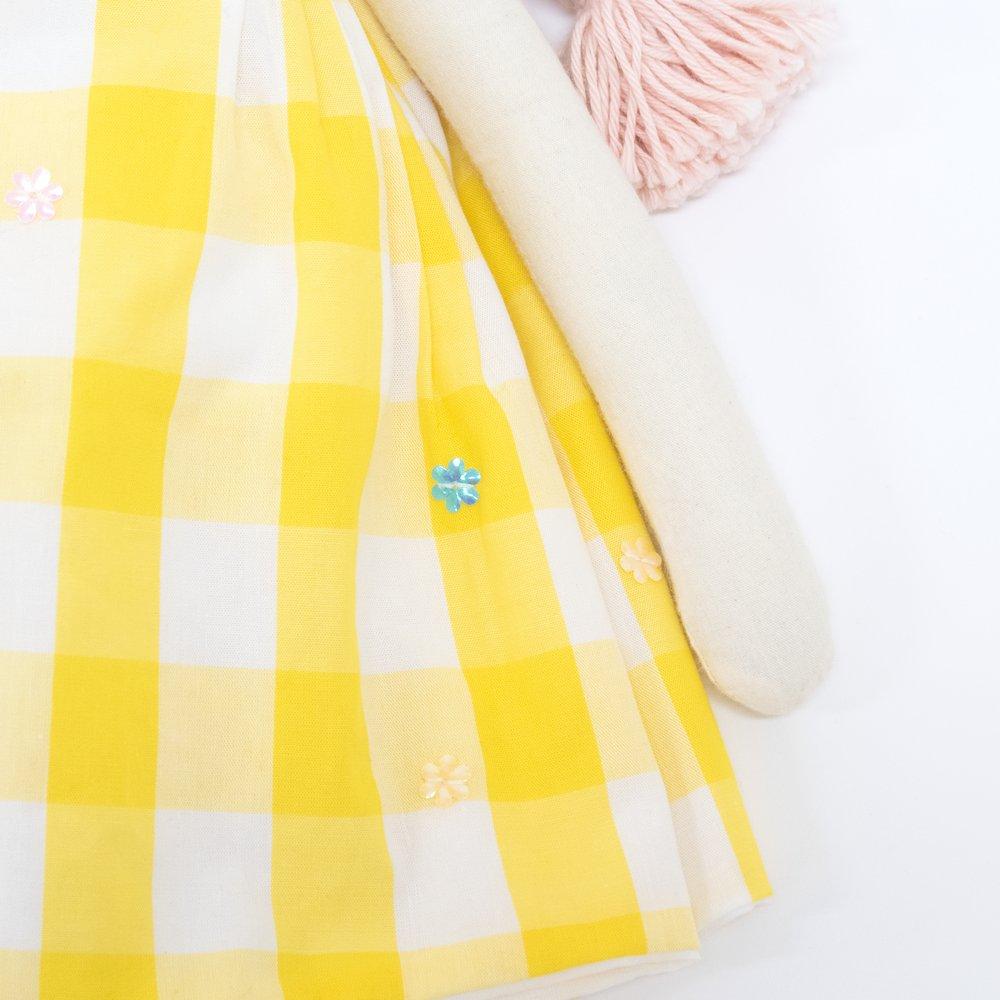 Alice is crafted from fabric, and is wearing a yellow gingham dress and a bunny ear headband. 