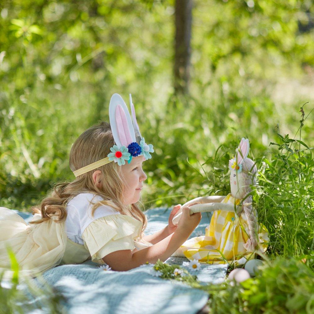 Alice is crafted from fabric, and is wearing a yellow gingham dress and a bunny ear headband. 